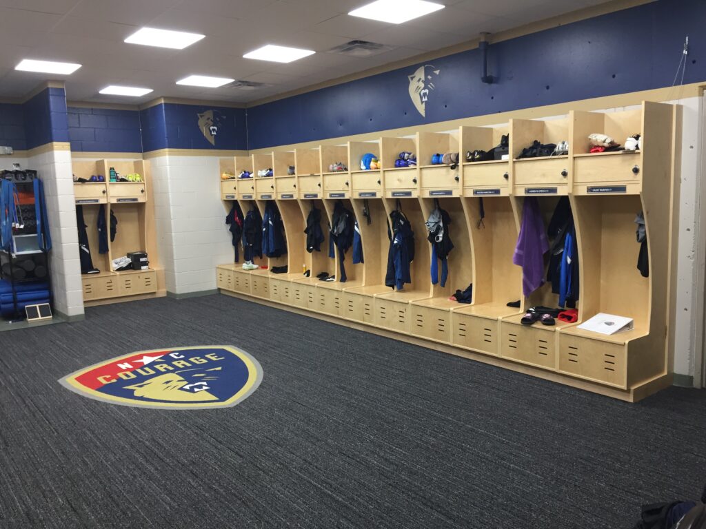 Renovated sports locker room with custom wooden lockers, carpet flooring, and modern lighting by Corner Solutions.