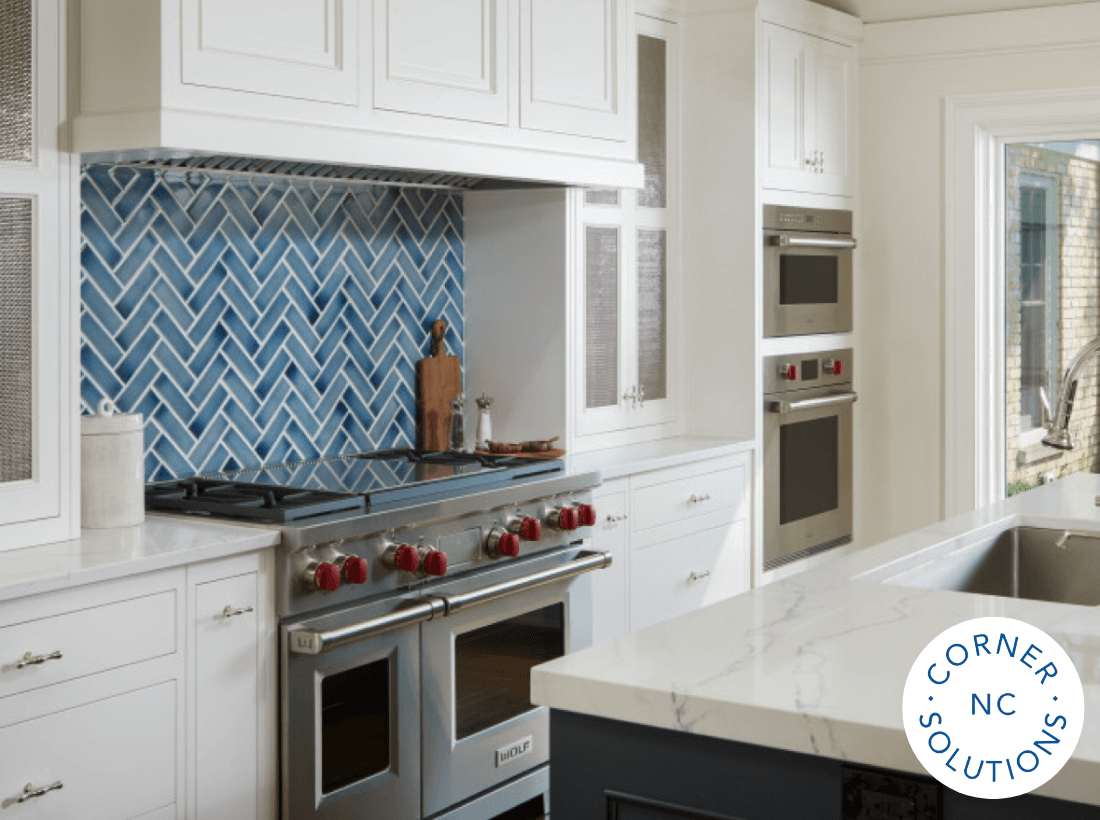 Modern kitchen renovation with blue herringbone tile backsplash, stainless steel double oven, gas range with red knobs, and white shaker-style cabinetry.